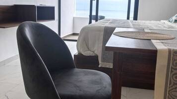 A modern hotel room with a large window, a flat-screen TV mounted on the wall, a wooden desk, and a comfortable chair.