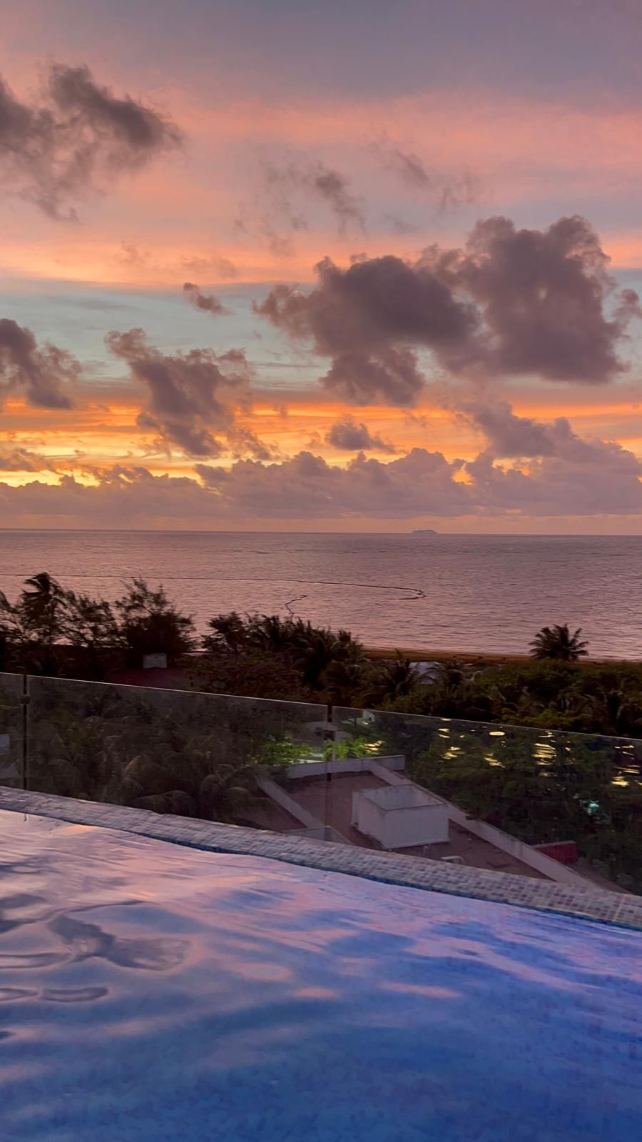 Una piscina en la azotea con vista al océano y al atardecer.