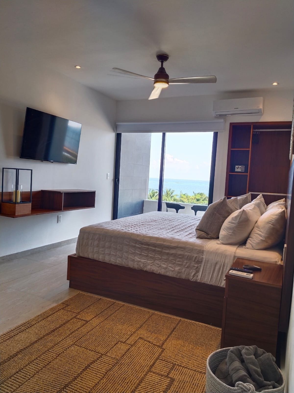 A bedroom with a bed, a television, a ceiling fan, and a view of the ocean.