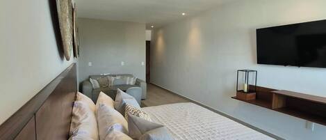 A modern bedroom with a large bed, a ceiling fan, a flat-screen TV, and a seating area with a sofa and a coffee table.