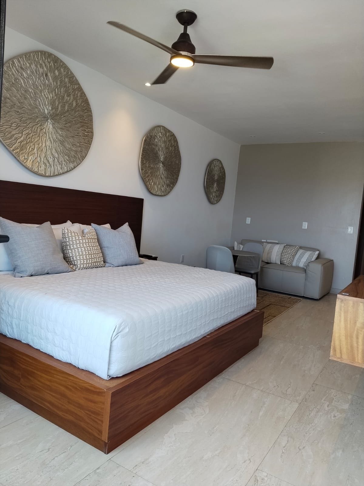 Une chambre avec un grand lit, un ventilateur de plafond et des œuvres d’art murales.
