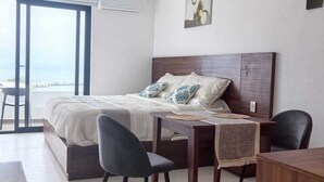 Ein modernes Schlafzimmer mit einem großen Bett, zwei Stühlen, einem Holztisch und Meerblick durch eine Glastür.