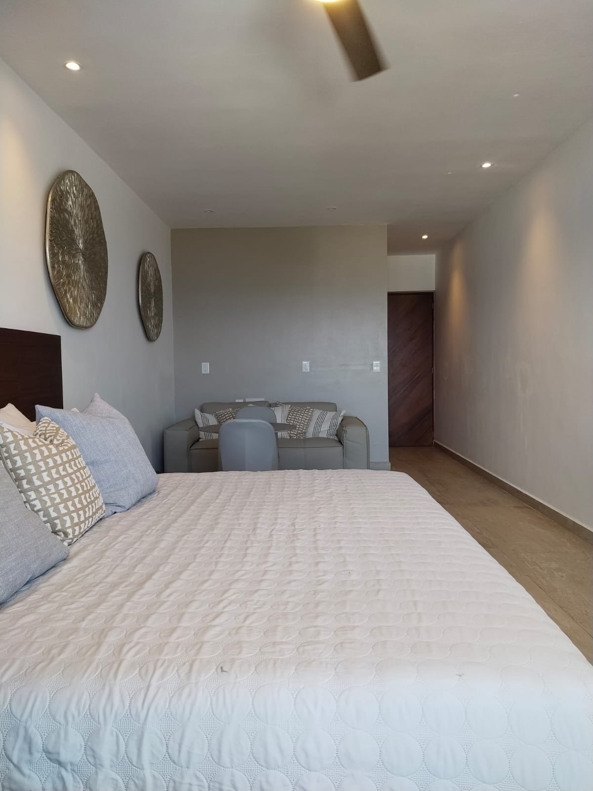 Un dormitorio moderno con una cama grande, una zona de estar con sofá y sillones, y un elemento decorativo en la pared.