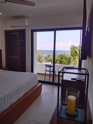 A bedroom with a bed, a desk, and a view of the ocean. - Miramare Ocean View (Puerto Morelos)