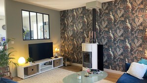 A living room with a TV, sofa, glass coffee table, and a fireplace. - Charming single-storey house (Évran)