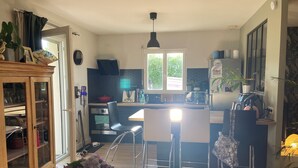 A modern kitchen with a central island, stainless steel appliances, and a dining area with chairs. - Charming single-storey house (Évran)