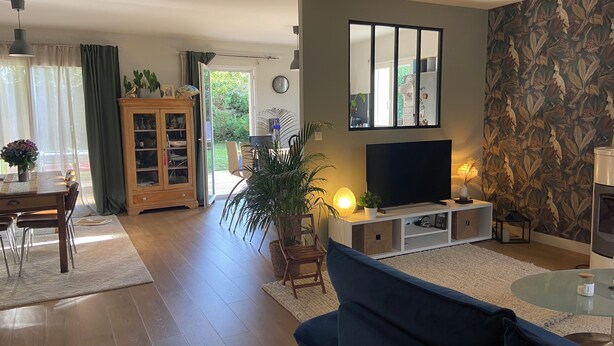 A living room with a TV, sofa, and a dining area with a table and chairs. - Charming single-storey house (Évran)