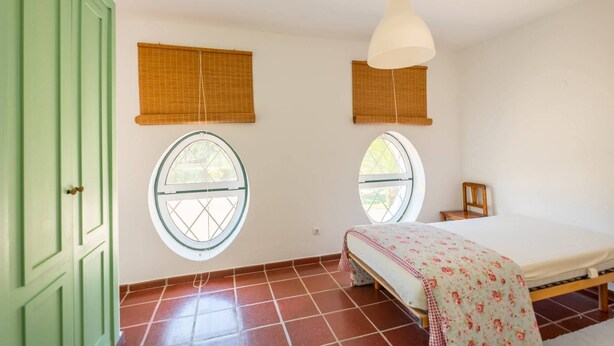 A room with a bed, two windows with blinds, a hanging light fixture, and a green door. - 188 - Quinta da Sobreda (Benavente)