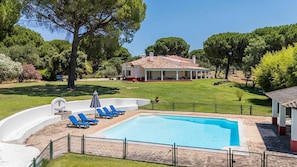 A swimming pool with lounge chairs, a covered patio, and a house with a red-tiled roof.