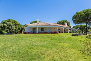 A single-story house with a tiled roof, a covered porch, and a grassy lawn.