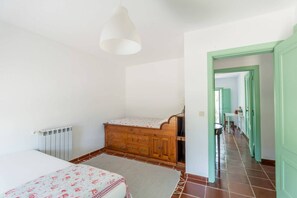 A bedroom with a bed, dresser, radiator, and a hallway leading to another room.