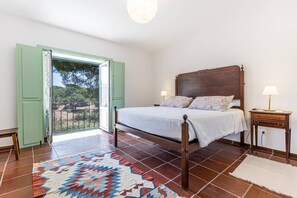 Un dormitorio con cama, mesita de noche, lámpara, alfombra estampada y puerta corrediza de vidrio que da a un espacio exterior.
