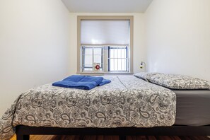 Een slaapkamer met een bed, een raam met zonwering, en een blauwe handdoek op het bed.