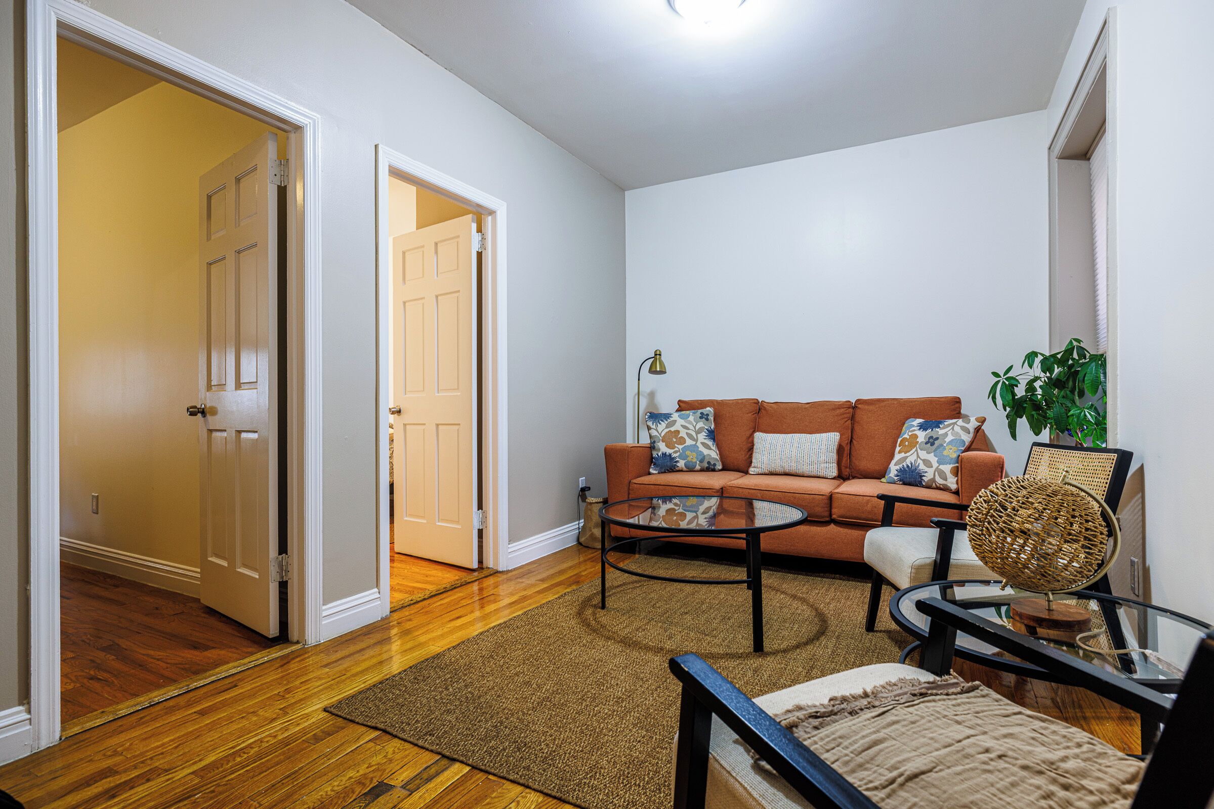 A living room with hardwood flooring, a brown sofa, a coffee table, and a wicker chair.