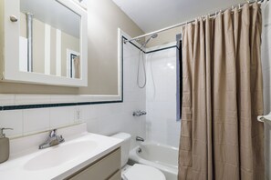 Een badkamer met een wit wastafelmeubel, toilet, bad en douchegordijn.