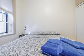 Una cama con ropa de cama estampada, una ventana con persianas y una lámpara de noche.