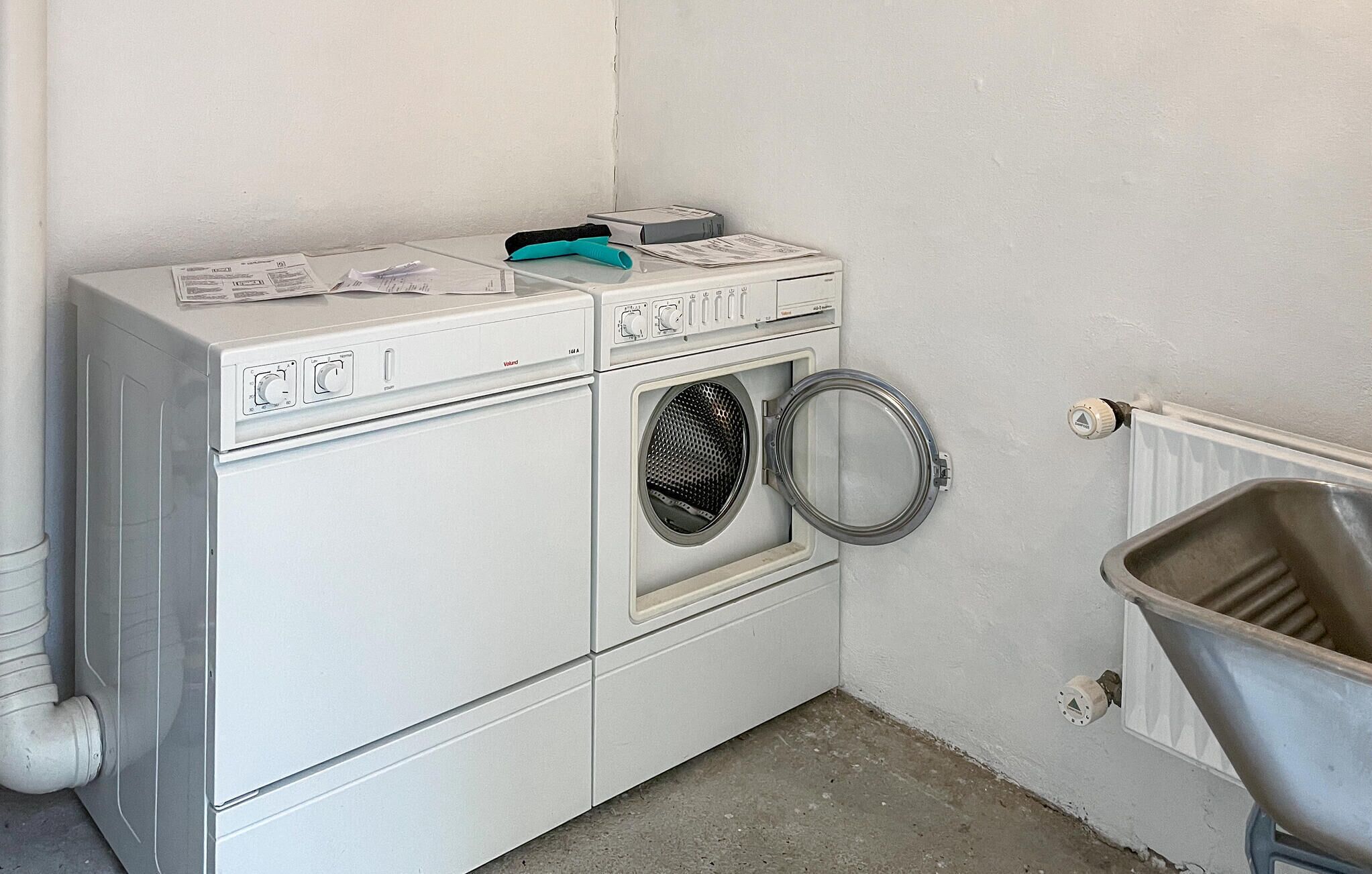 A compact laundry area with a front-loading washing machine, a dryer, and a metal trash bin.