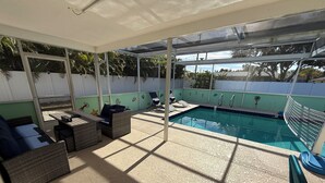 Ett takförsett utomhusområde med en pool, solstolar och en sittgrupp med kuddar.