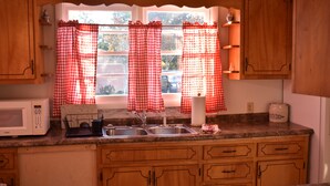 Cozinha com armários de madeira, micro-ondas, pia e janela com cortinas xadrez vermelhas.