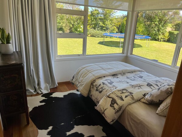 Un dormitorio con un ventanal grande, un tapete de cuero de vaca, una cama con ropa de cama estampada y una mesita con una planta.