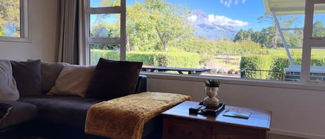A living room with a sofa, a coffee table, and a view of a mountainous landscape through large windows.