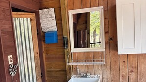 A rustic cabin interior with a wooden interior, a white sink, and a mirror above it. - Site 3 Private camp power @ site w Hot Showers & Potty At The CommunityBathhouse (Smithville)
