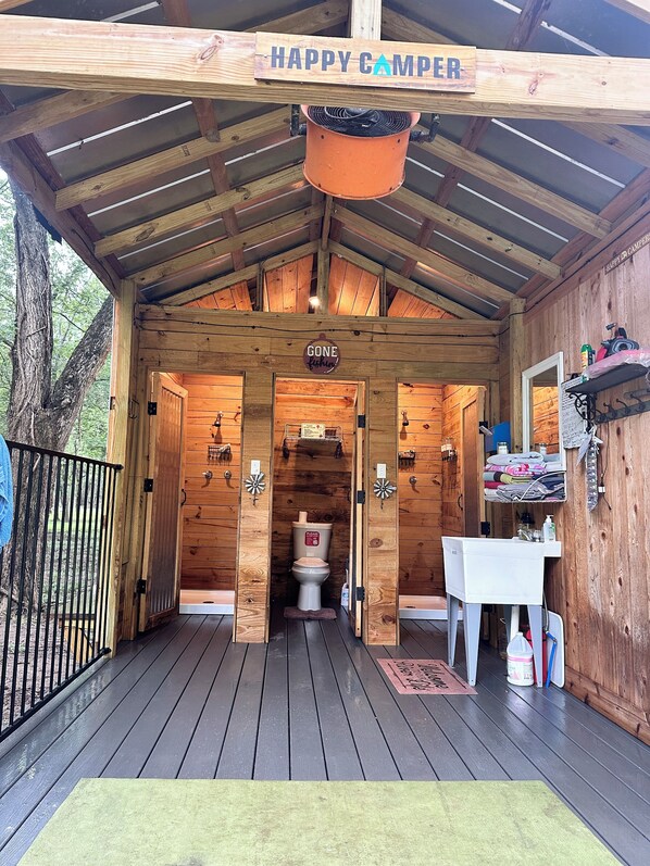 A wooden cabin with a 'Happy Camper' sign, a 'Gone Fishing' sign, and a small bathroom with a toilet and sink.