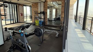 Un gimnasio con equipo de ejercicio, grandes ventanales y vistas a la ciudad.