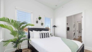 Un dormitorio moderno con una cama grande, una planta en maceta y vistas a un área de lavandería.