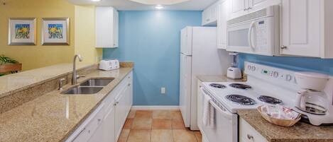 A kitchen with white cabinets, a granite countertop, a sink, a stove, and a microwave.