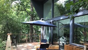 Une terrasse en bois avec un espace patio fermé par des parois de verre, un parasol bleu et une chaise.