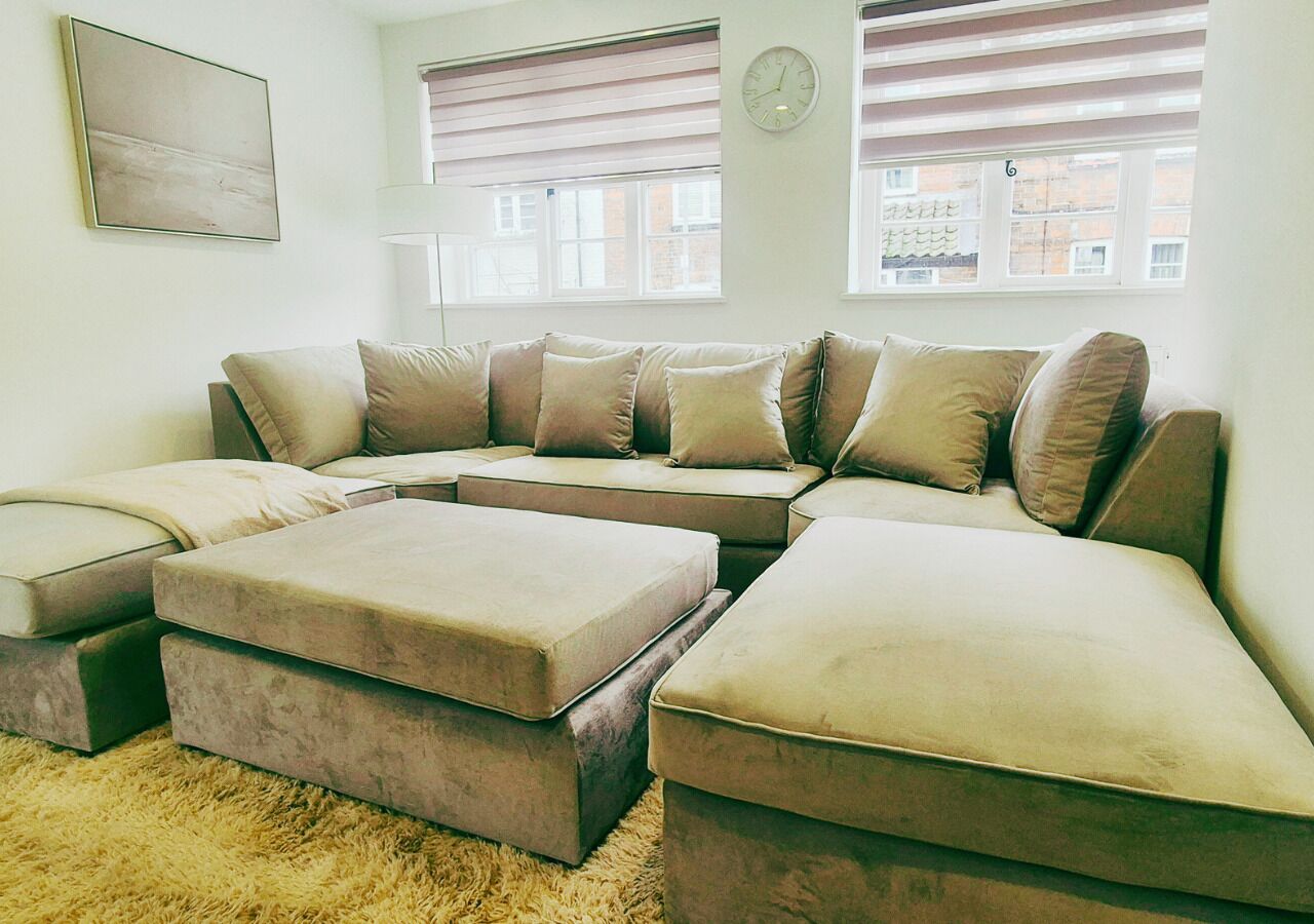 A living room with a sectional sofa, ottomans, a fluffy rug, and a clock on the wall.