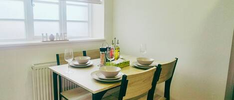 A dining table with four chairs, a window with blinds, a radiator, and a 'HOME' sign on the wall.