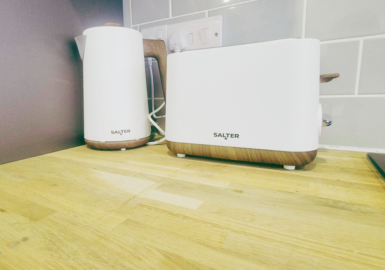Two white electric kettles with wooden bases on a wooden countertop.