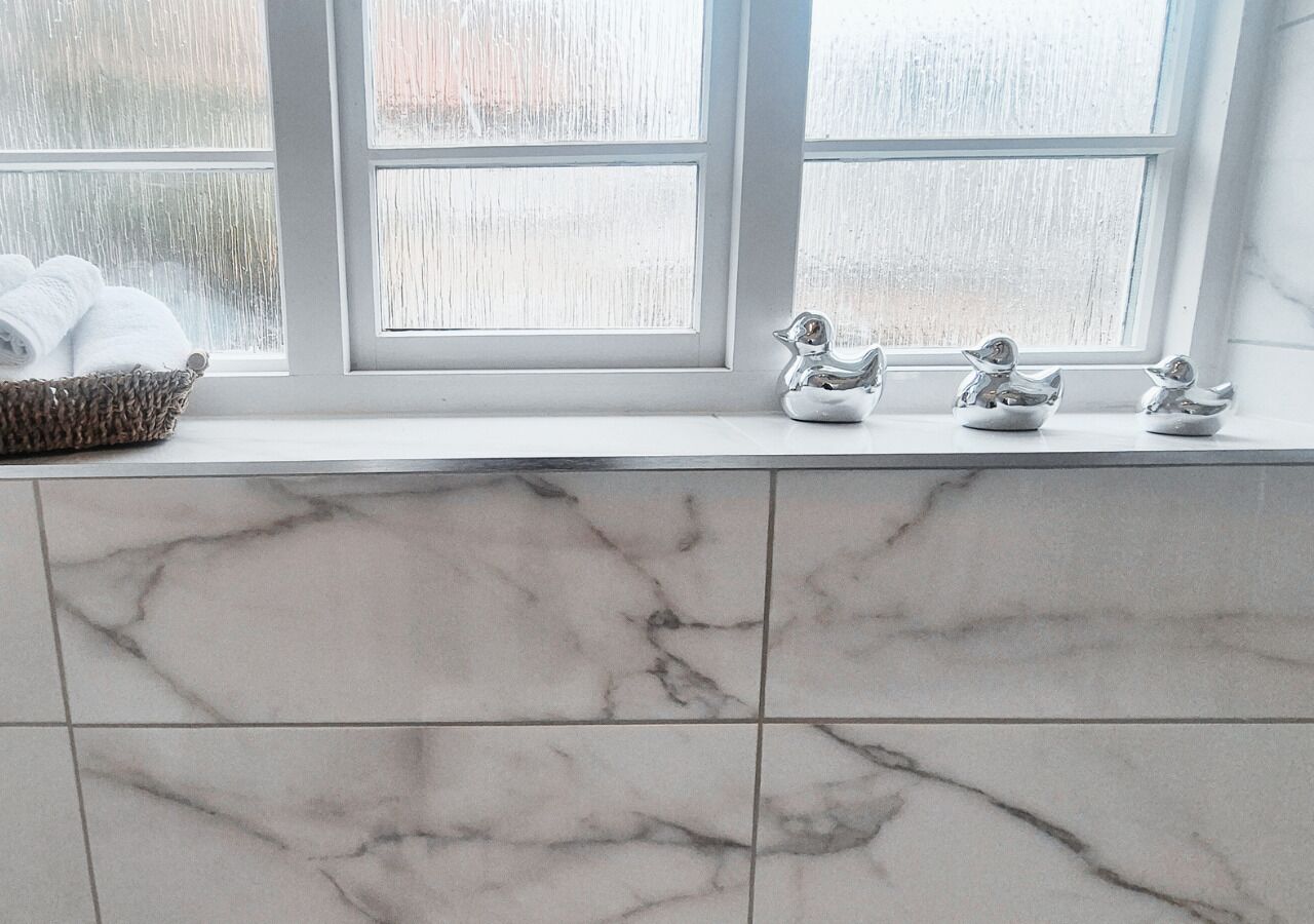 Une salle de bain carrelée de marbre, une fenêtre avec vue et un panier rempli de serviettes.