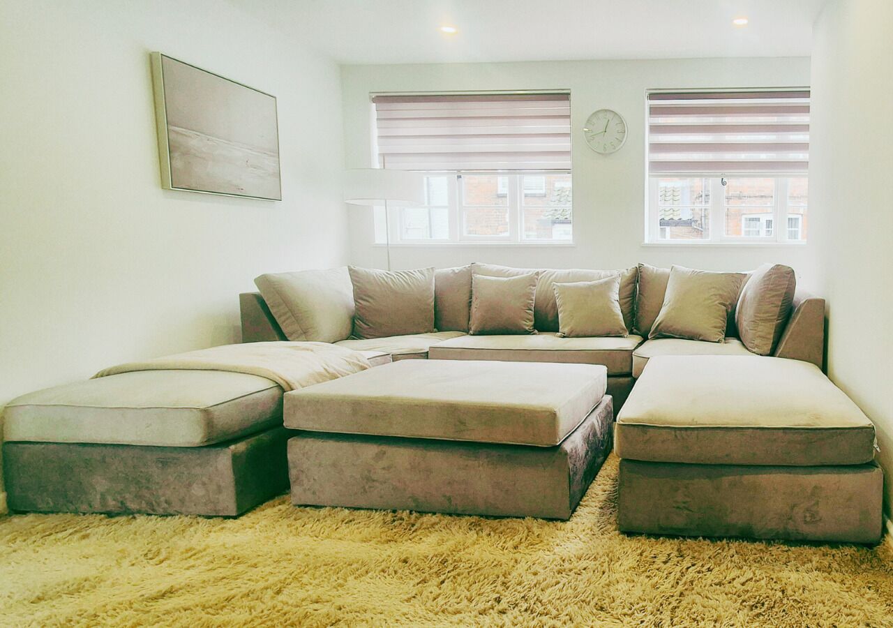 A living room with a sectional sofa, ottomans, a fluffy rug, and a clock on the wall.