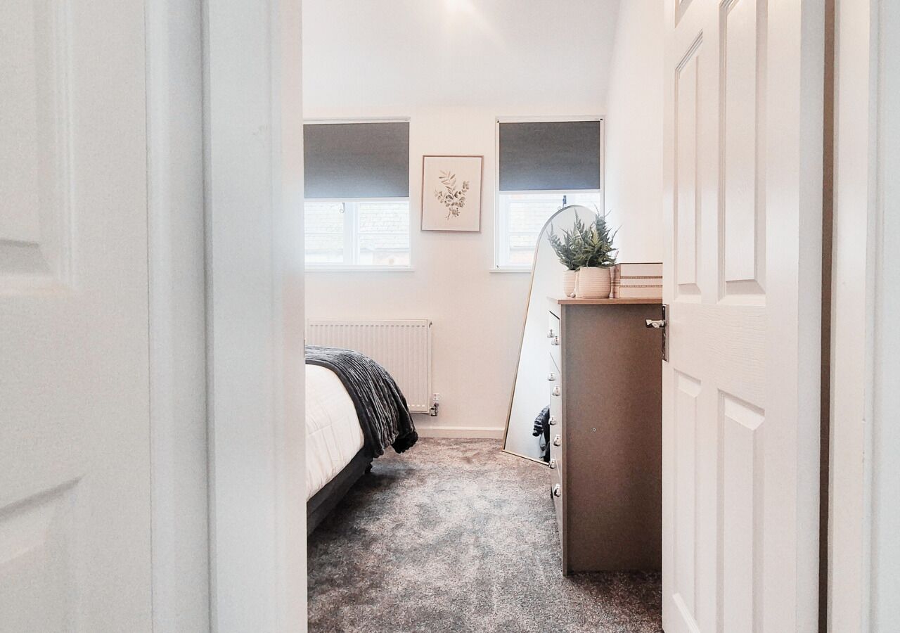 Une chambre à coucher avec un lit, une commode, un radiateur et une fenêtre avec des stores.