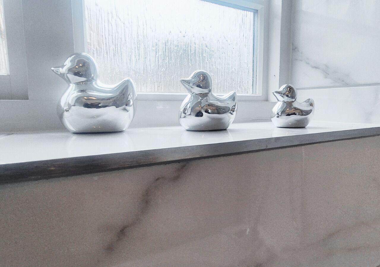 Three silver duck-shaped vases on a marble countertop near a window.