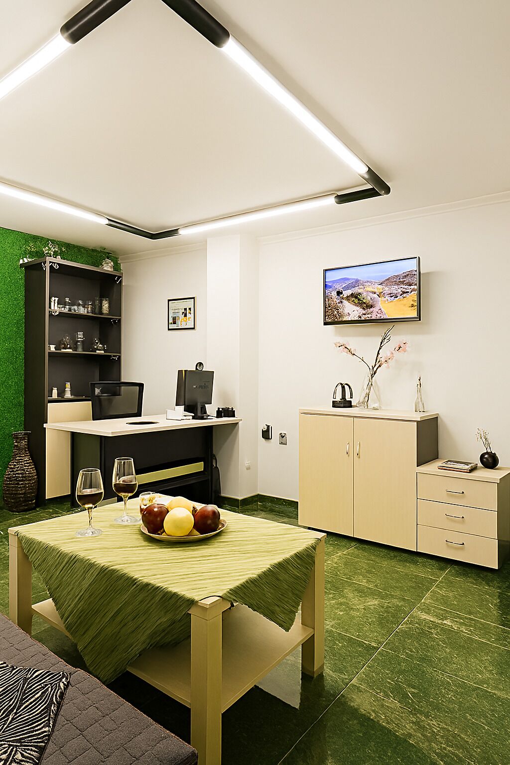 A modern kitchen with a dining area, green wall, and a flat-screen TV.