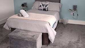 Un dormitorio con una cama, una mesita de noche, una lámpara y un enchufe en la pared.