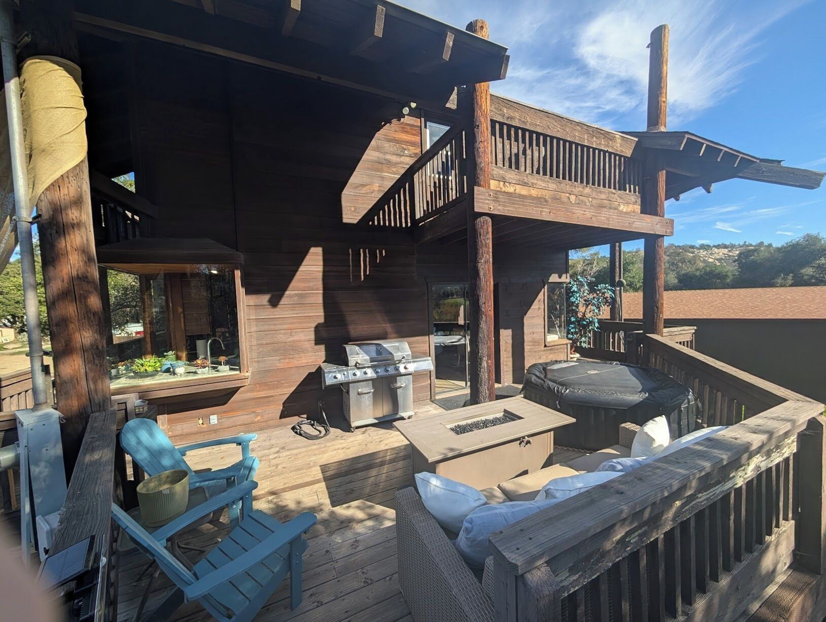 A wooden deck with a grill, outdoor seating, and a view of the surrounding landscape.