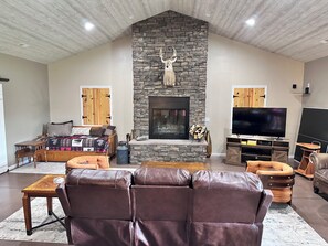 A living room with a stone fireplace, leather sofa, TV, and wooden accents. - Family Retreat with pool table and double bunks. (Bethany)