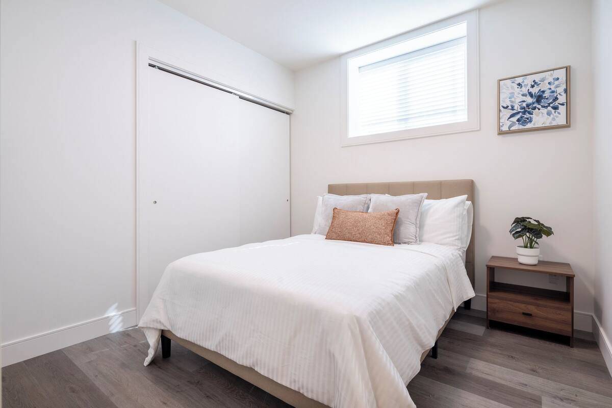 A bedroom with a bed, a nightstand with a plant, a window, and a door.