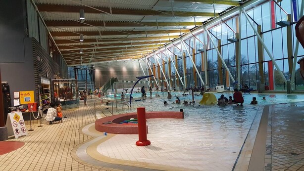 Une piscine intérieure dotée de plusieurs couloirs de nage, d’une plateforme de plongeon et d’un toboggan.