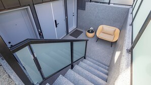 Un espace extérieur moderne avec une balustrade en verre, une chaise beige et une petite table agrémentée d’une plante.