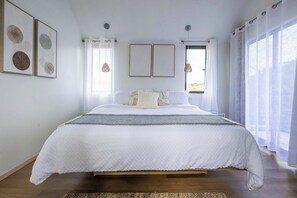 Ein Schlafzimmer mit einem großen Bett, zwei Nachttischen, einem Fenster mit Vorhängen und Wandbildern.
