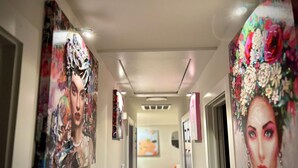 En gang med kunst på væggene, en dør til højre og et bord med stole i baggrunden.