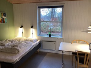 A bedroom with a bed, bedside lamps, a window with a view of trees, a radiator, and a small table with a chair. - 2 Person Holiday Home in Ansager (Ansager)