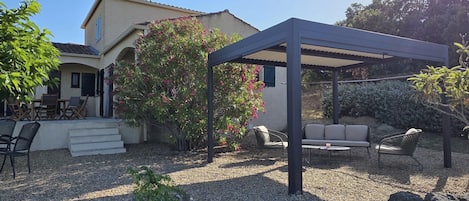 A covered patio area with outdoor furniture, a pergola, and a garden with various plants and a tree.