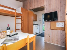 Una habitación compacta con literas, una pequeña cocina, un televisor y un tablón de anuncios.